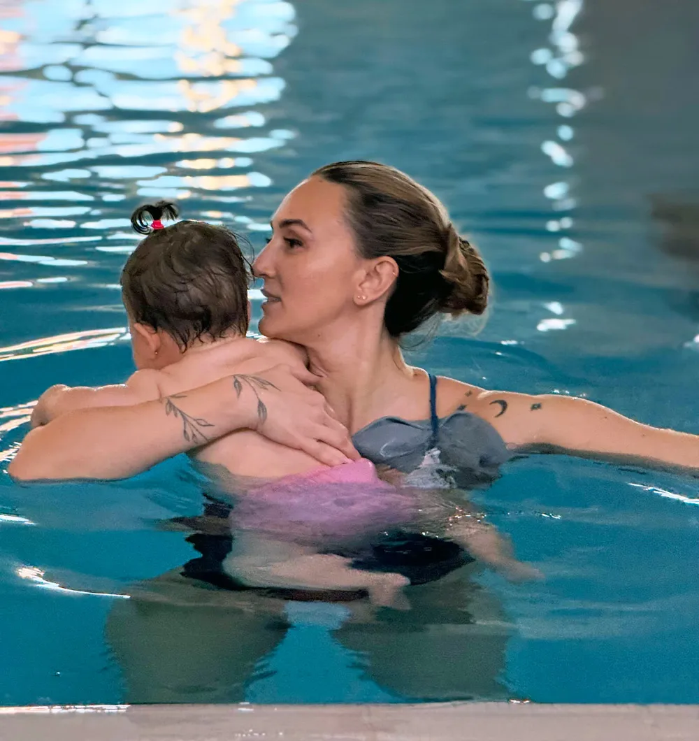 Antrenoare Swim Factory cu un bebeluș în brațe, în bazin, la Aquabebe